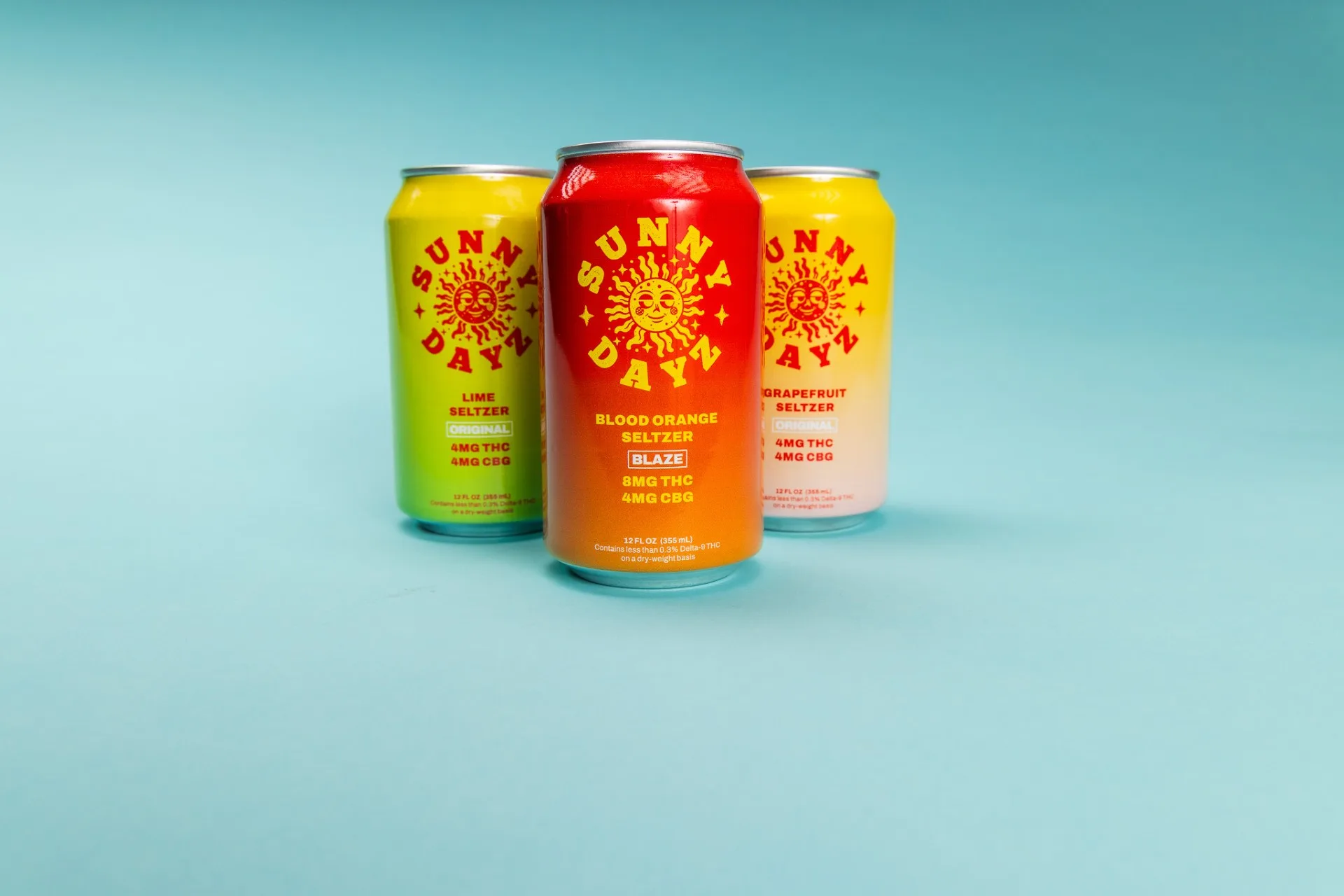 Three Sunny Dayz hemp-derived THC seltzer cans on a blue background: lime and grapefruit at 4mg THC and 4mg CBG, and blood orange Blaze at 8mg THC and 4mg CBG, each labeled as containing less than 0.3% delta-9 THC on a dry-weight basis.